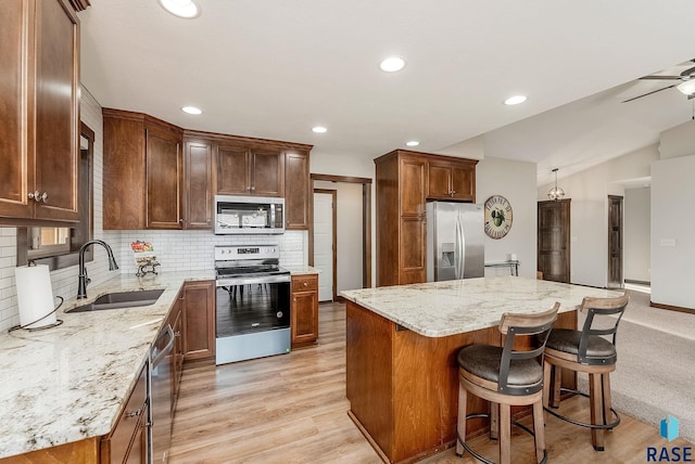 kitchen featuring a center island, a sink, stainless steel appliances, light stone countertops, and tasteful backsplash