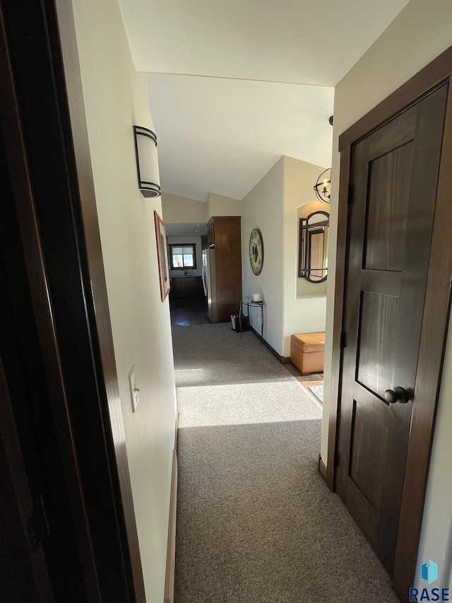 hall with lofted ceiling, a notable chandelier, light carpet, and baseboards
