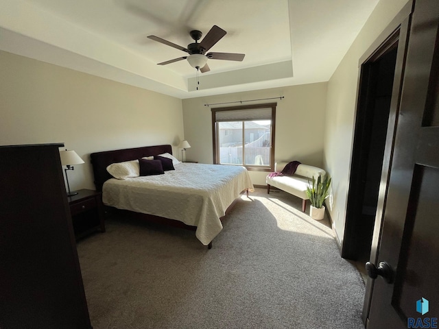 carpeted bedroom with a raised ceiling and ceiling fan