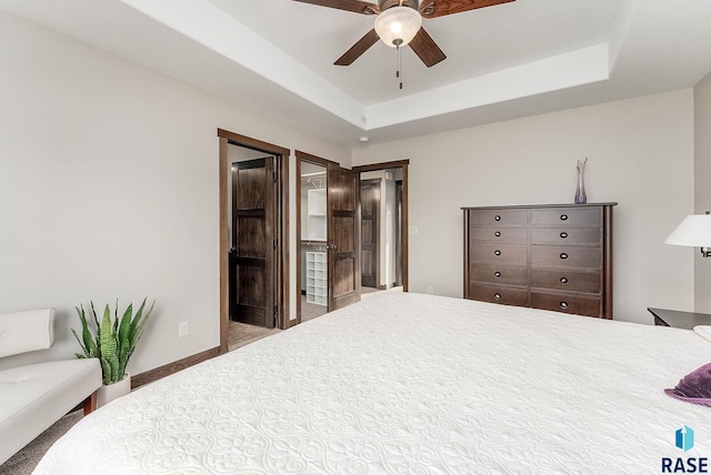 carpeted bedroom featuring a tray ceiling and a ceiling fan