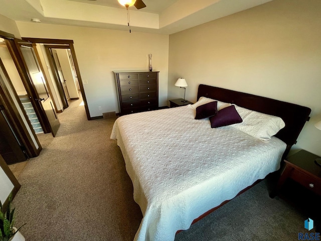 bedroom with a ceiling fan, baseboards, a tray ceiling, and light colored carpet