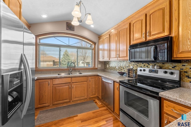 kitchen with a sink, appliances with stainless steel finishes, backsplash, light wood-style floors, and lofted ceiling