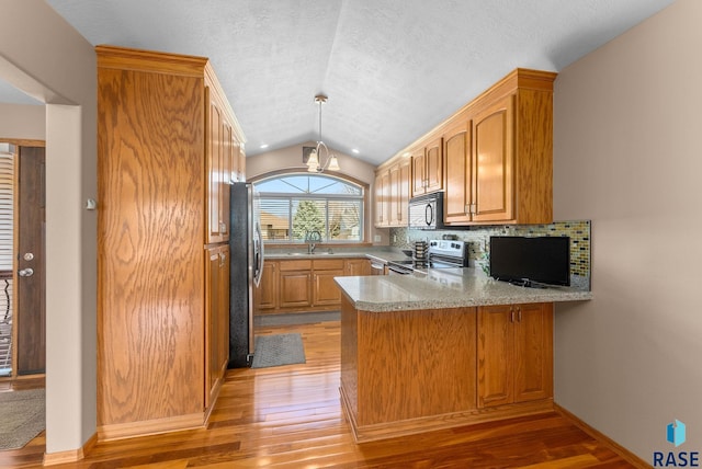 kitchen featuring lofted ceiling, light wood-style flooring, a sink, a peninsula, and appliances with stainless steel finishes