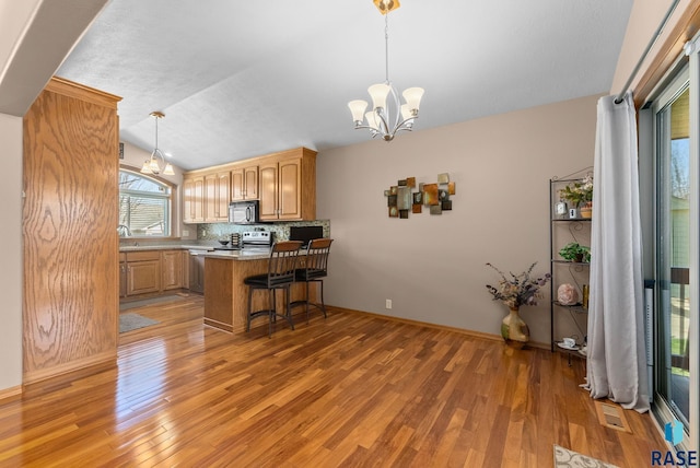 kitchen with a chandelier, a peninsula, black microwave, and light wood-style floors