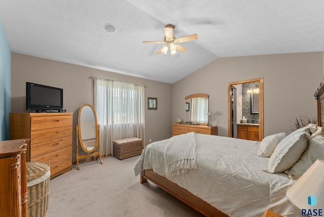 bedroom featuring light carpet, lofted ceiling, ensuite bath, and a ceiling fan
