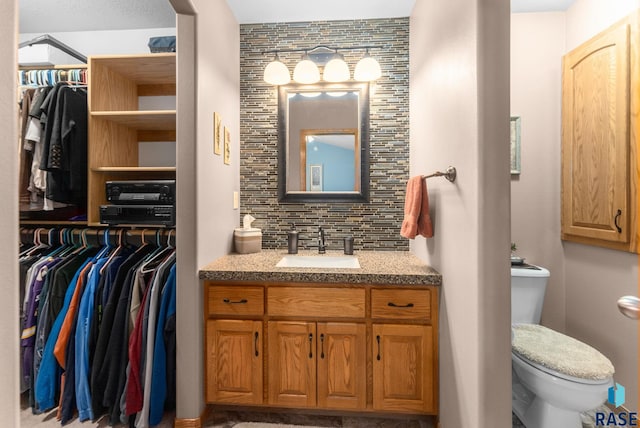 bathroom featuring toilet, a spacious closet, tasteful backsplash, and vanity