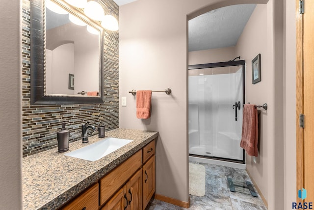 full bath with baseboards, vanity, decorative backsplash, and a shower stall