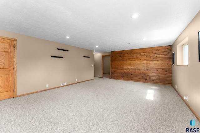 spare room featuring carpet flooring, wood walls, baseboards, and recessed lighting