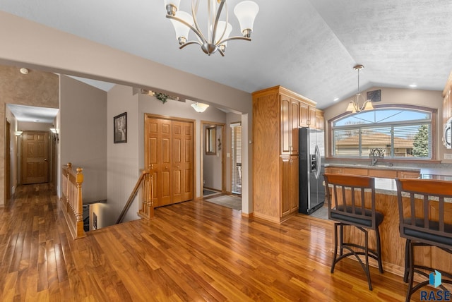 kitchen featuring wood-type flooring, a sink, stainless steel appliances, a notable chandelier, and vaulted ceiling