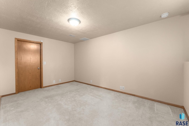 spare room with a textured ceiling, light carpet, baseboards, and visible vents