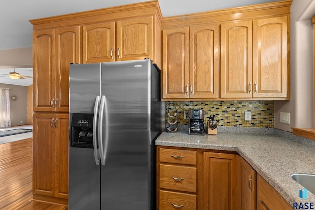 kitchen featuring light stone counters, tasteful backsplash, stainless steel refrigerator with ice dispenser, and wood finished floors