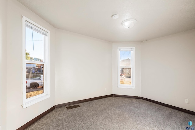 carpeted empty room with baseboards, plenty of natural light, and visible vents