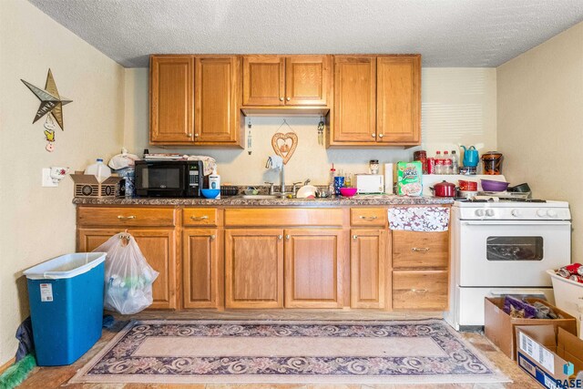 kitchen with a textured ceiling, a sink, black microwave, white gas stove, and brown cabinets