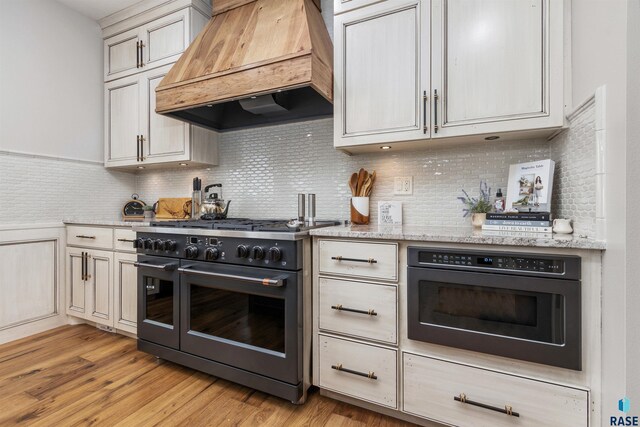 5604 S Jersey Tess Dr, Sioux Falls, SD 57108 - kitchen featuring black oven, light wood finished floors, decorative backsplash, double oven range, and custom range hood