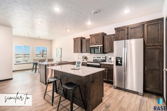 6218 S Tanner Ave, Sioux Falls, SD 57108 - kitchen featuring a sink, stainless steel appliances, a kitchen breakfast bar, dark brown cabinetry, and light wood-style floors