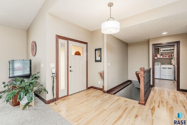 foyer entrance featuring washer and dryer, light wood finished floors, and baseboards