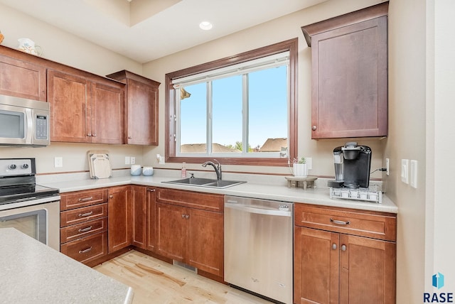 kitchen featuring stainless steel appliances, a sink, light wood finished floors, light countertops, and brown cabinetry