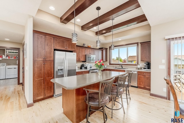 kitchen with stainless steel appliances, washing machine and clothes dryer, light wood-style floors, a sink, and beamed ceiling