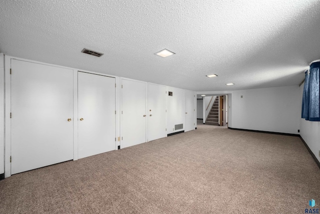 finished below grade area with carpet, a textured ceiling, visible vents, and stairs
