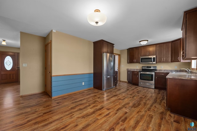 kitchen with dark wood-style flooring, appliances with stainless steel finishes, a sink, and dark brown cabinetry