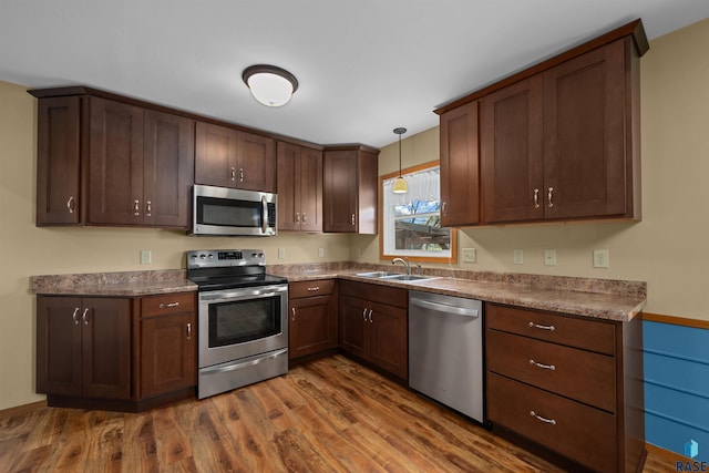 kitchen featuring hanging light fixtures, a sink, dark brown cabinetry, appliances with stainless steel finishes, and dark wood-style floors
