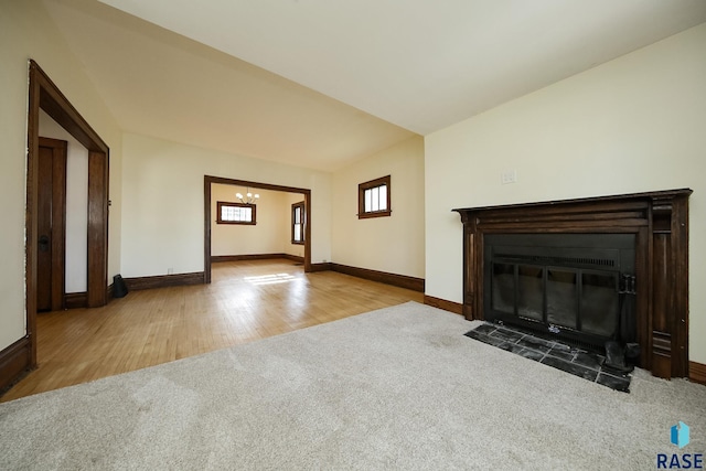 unfurnished living room with an inviting chandelier, baseboards, a fireplace with flush hearth, and carpet floors