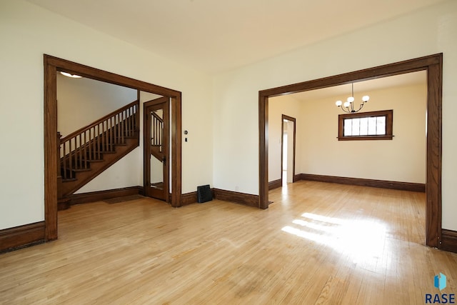spare room featuring light wood-style floors, a chandelier, baseboards, and stairway