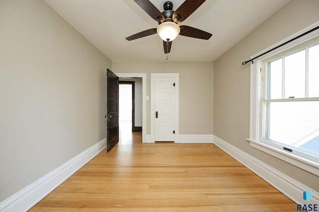 spare room featuring light wood finished floors, baseboards, a ceiling fan, and plenty of natural light