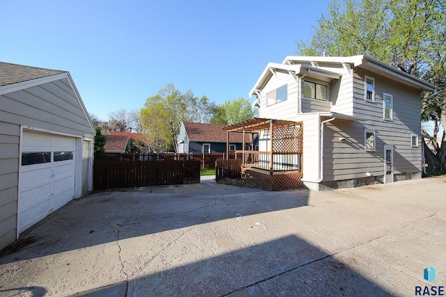 view of home's exterior with fence, a garage, a pergola, concrete driveway, and a deck