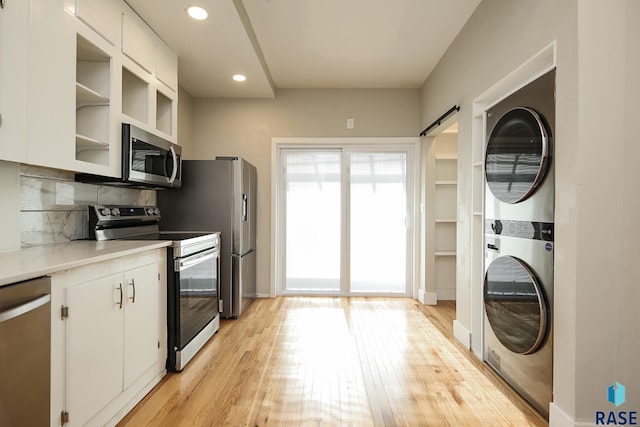 kitchen featuring appliances with stainless steel finishes, stacked washer / drying machine, white cabinetry, backsplash, and light wood-type flooring