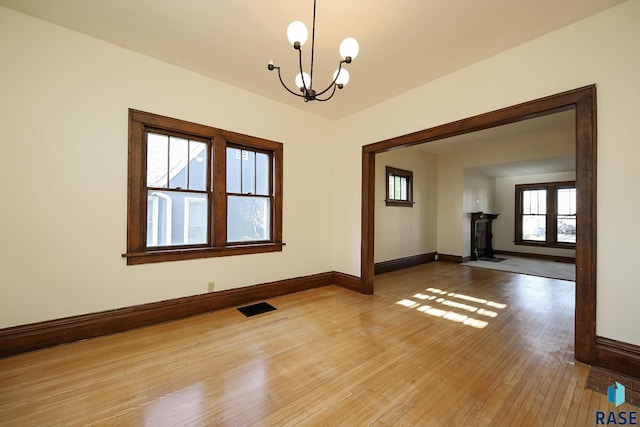 unfurnished room featuring light wood finished floors, a notable chandelier, visible vents, baseboards, and a wood stove