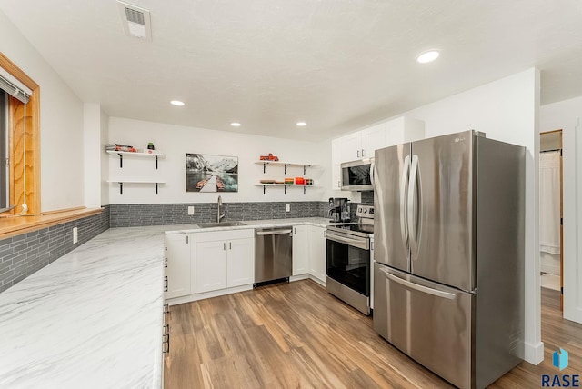 kitchen featuring a sink, open shelves, stainless steel appliances, visible vents, and light stone countertops