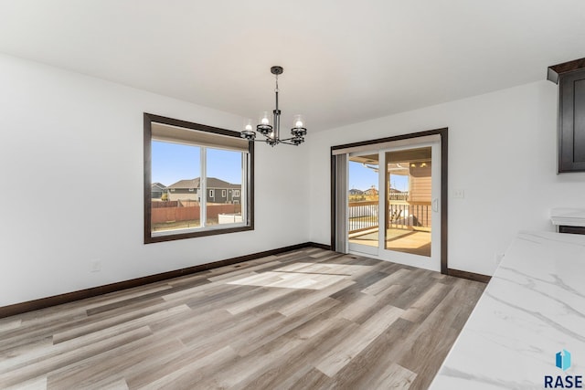 unfurnished dining area with a chandelier, baseboards, plenty of natural light, and light wood-style floors
