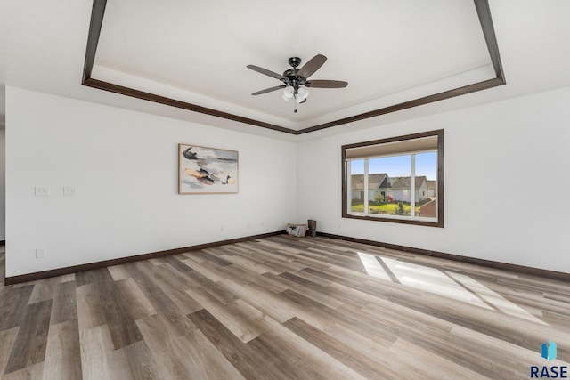 unfurnished room featuring a ceiling fan, a raised ceiling, baseboards, and wood finished floors