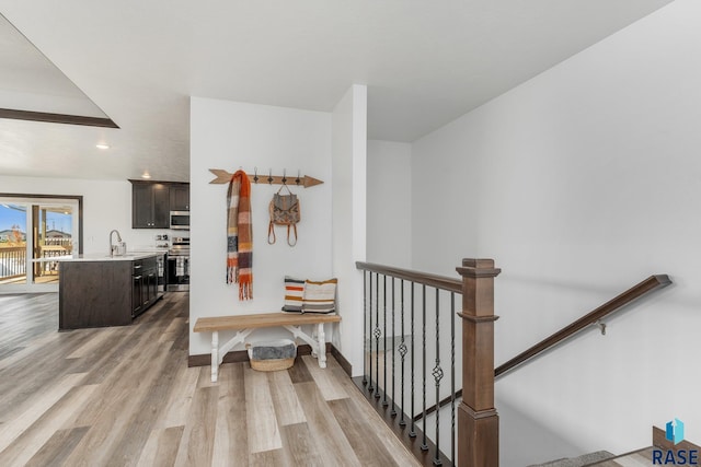 hallway featuring an upstairs landing, a sink, baseboards, light wood-style floors, and recessed lighting