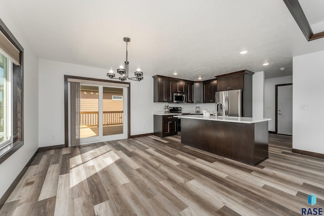kitchen featuring stainless steel appliances, light wood-type flooring, dark brown cabinetry, light countertops, and a notable chandelier