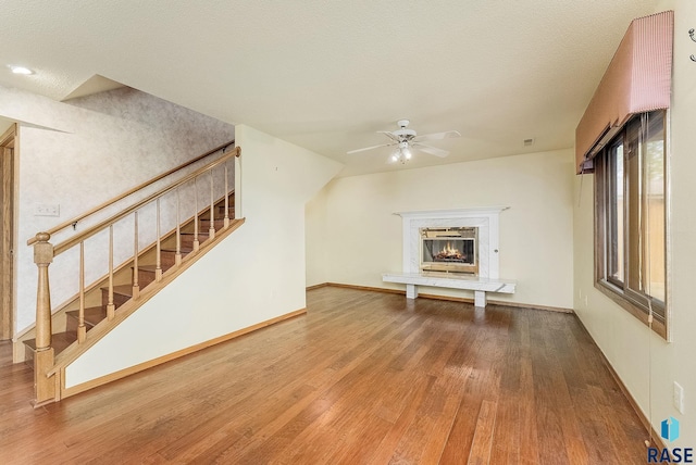 unfurnished living room featuring baseboards, ceiling fan, wood-type flooring, a high end fireplace, and stairway
