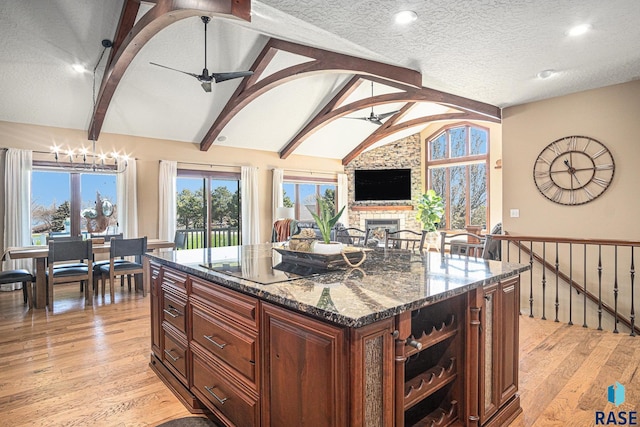 6601 Lenola Hts, Wentworth, SD 57075 - kitchen featuring light wood-style flooring, dark stone counters, lofted ceiling with beams, a stone fireplace, and black electric cooktop