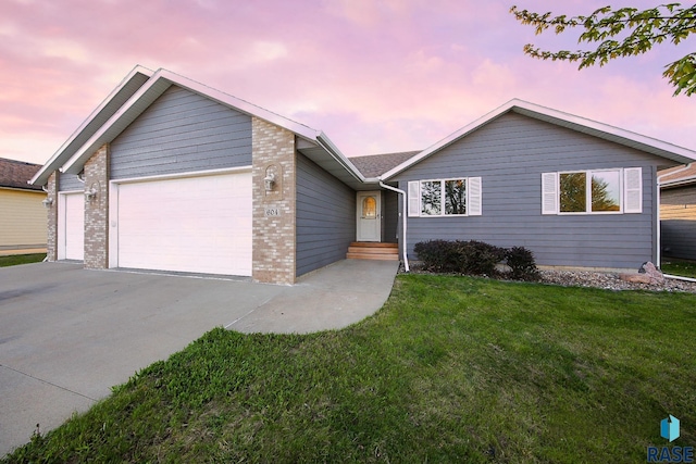 ranch-style home with a lawn, driveway, brick siding, and a garage