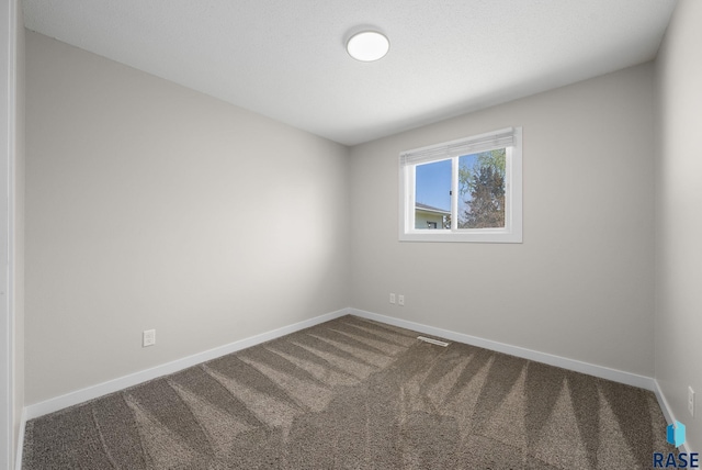 spare room featuring dark colored carpet, baseboards, and visible vents