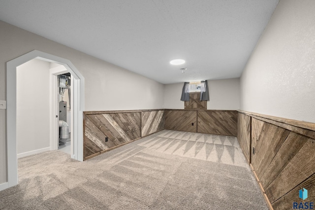 finished basement featuring arched walkways, wood walls, wainscoting, and carpet