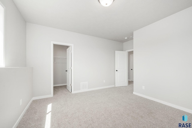 unfurnished bedroom featuring a spacious closet, carpet flooring, baseboards, and visible vents