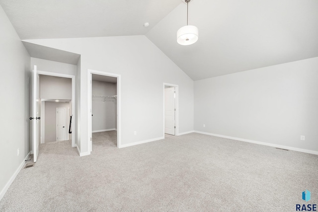 unfurnished bedroom featuring vaulted ceiling, a walk in closet, light carpet, and baseboards