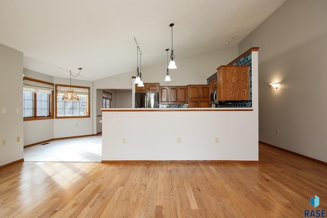 kitchen with brown cabinetry, light wood finished floors, stainless steel appliances, and vaulted ceiling