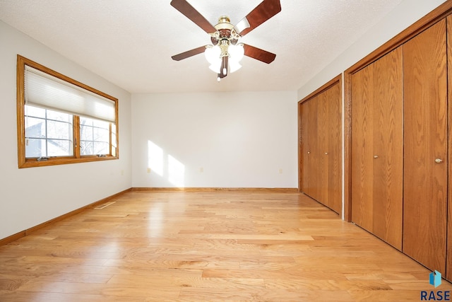unfurnished bedroom featuring light wood-style flooring, a ceiling fan, two closets, visible vents, and baseboards