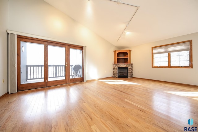 unfurnished living room with lofted ceiling, french doors, track lighting, a fireplace, and light wood-style flooring