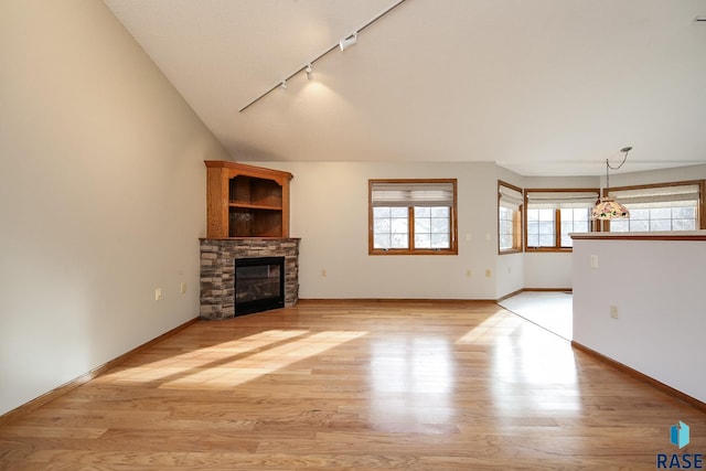 unfurnished living room featuring track lighting, a wealth of natural light, vaulted ceiling, and a fireplace