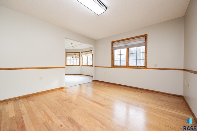 spare room with a chandelier, baseboards, and hardwood / wood-style flooring