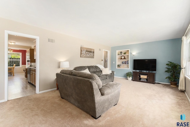 living room with baseboards, built in features, visible vents, and light colored carpet