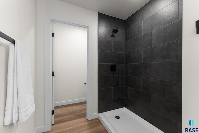 full bathroom featuring baseboards, wood finished floors, and a tile shower